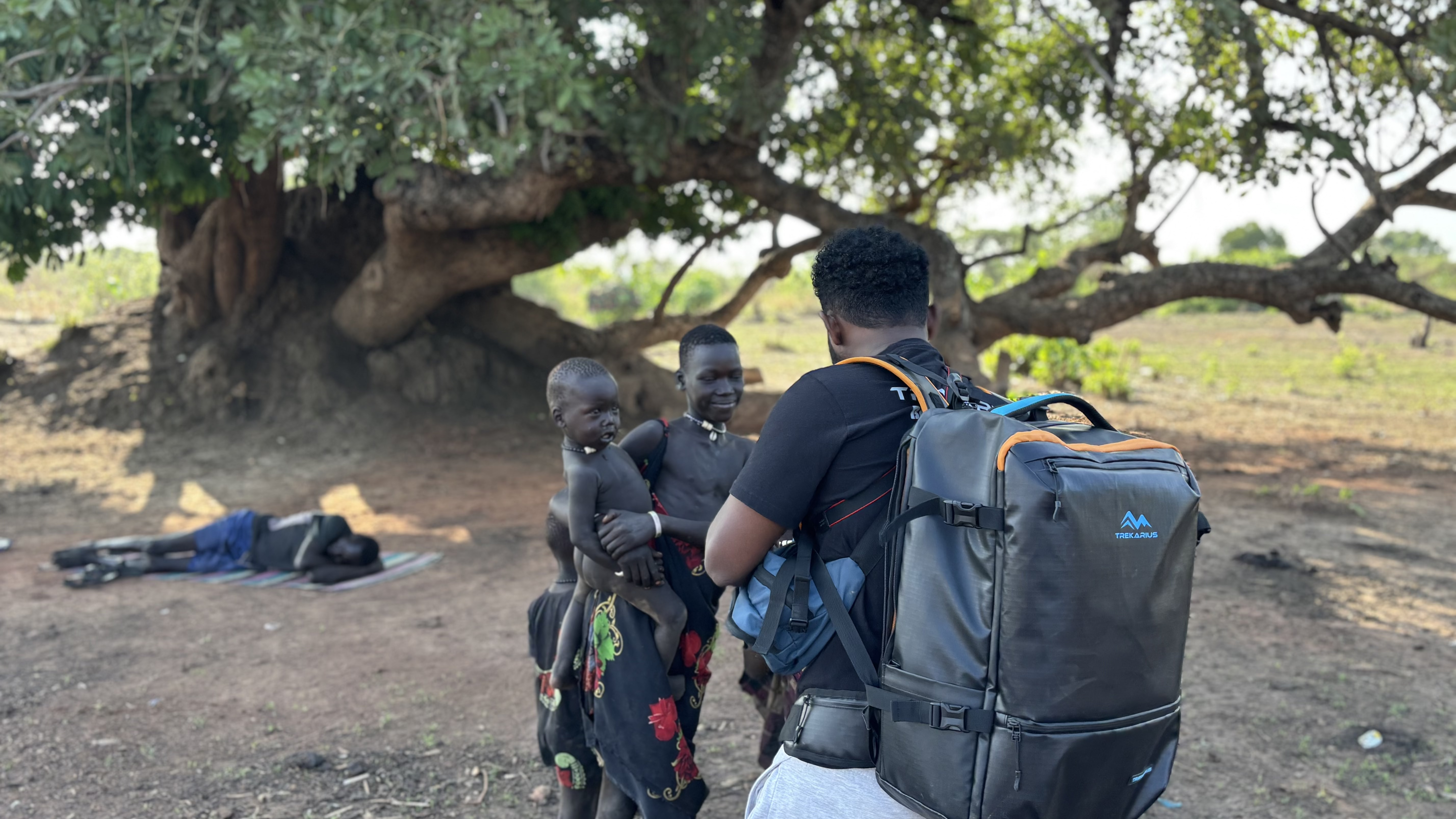 TREKARIUS 35L travel backpack with a filmmaker standing under a tree with children in a village in South Sudan