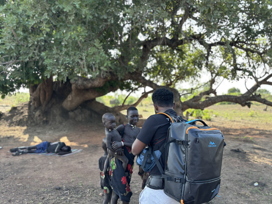 Person with the trekarius 35L travel backpack in a village in south sudan standing under a large tree with two children filming 